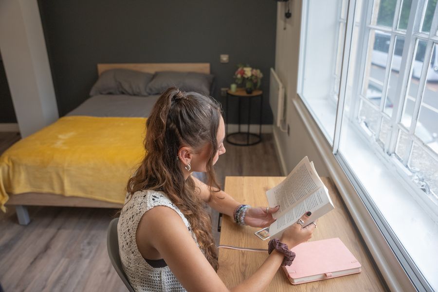 A student reading at the study desk beside the window of a studio